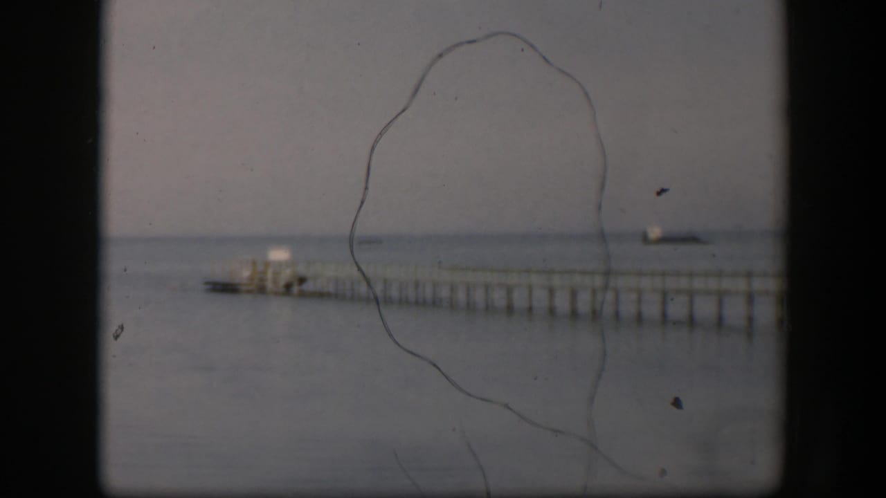 1951 Utah 8mm still showing the dock, small boat, calm water, horizon line, and prominent film scratches across the frame.