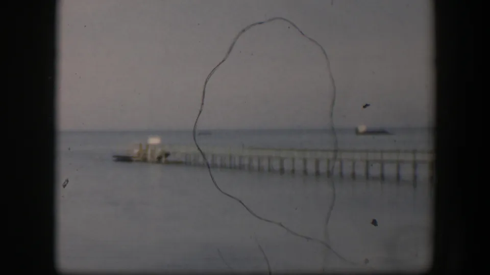 1951 Utah 8mm still showing the dock, small boat, calm water, horizon line, and prominent film scratches across the frame.