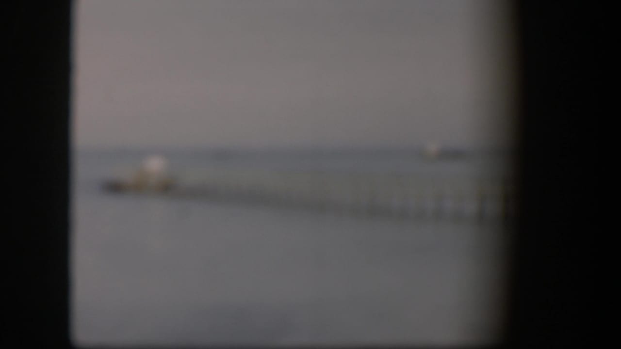 Soft-focus 1951 Utah frame with a dock and small boat faintly visible on calm water through dark 8mm frame edges.