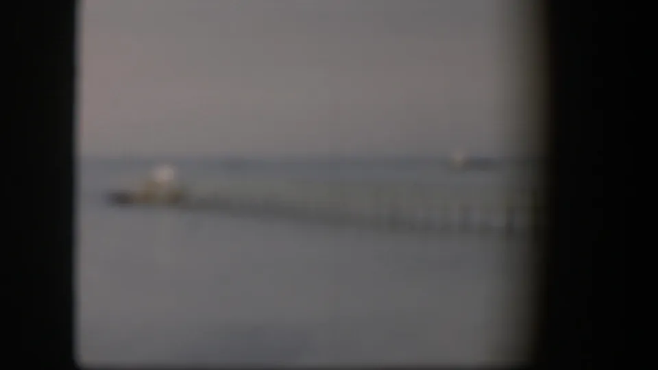 Soft-focus 1951 Utah frame with a dock and small boat faintly visible on calm water through dark 8mm frame edges.