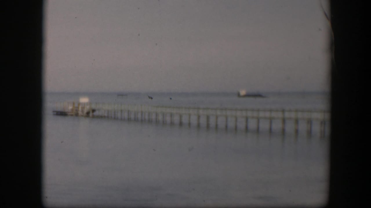 1951 Utah 8mm frame showing a long narrow pier or wharf stretching across calm water under a muted, hazy sky.