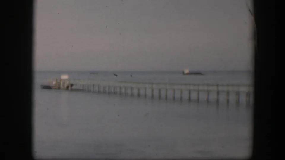 1951 Utah 8mm frame showing a long narrow pier or wharf stretching across calm water under a muted, hazy sky.