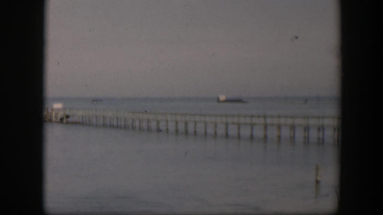 1951 Utah home-movie frame of a long pier over still water, with a small distant vessel-like shape near the hazy horizon.