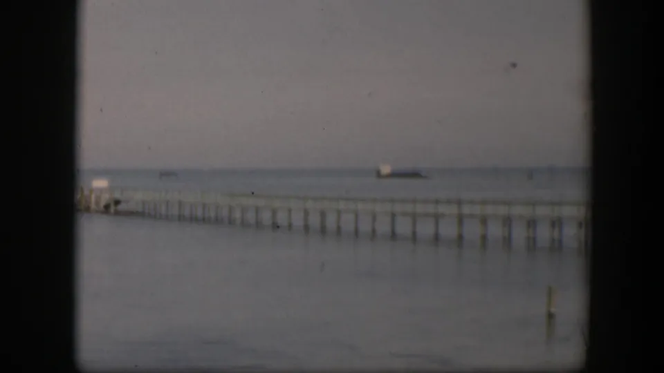 1951 Utah home-movie frame of a long pier over still water, with a small distant vessel-like shape near the hazy horizon.