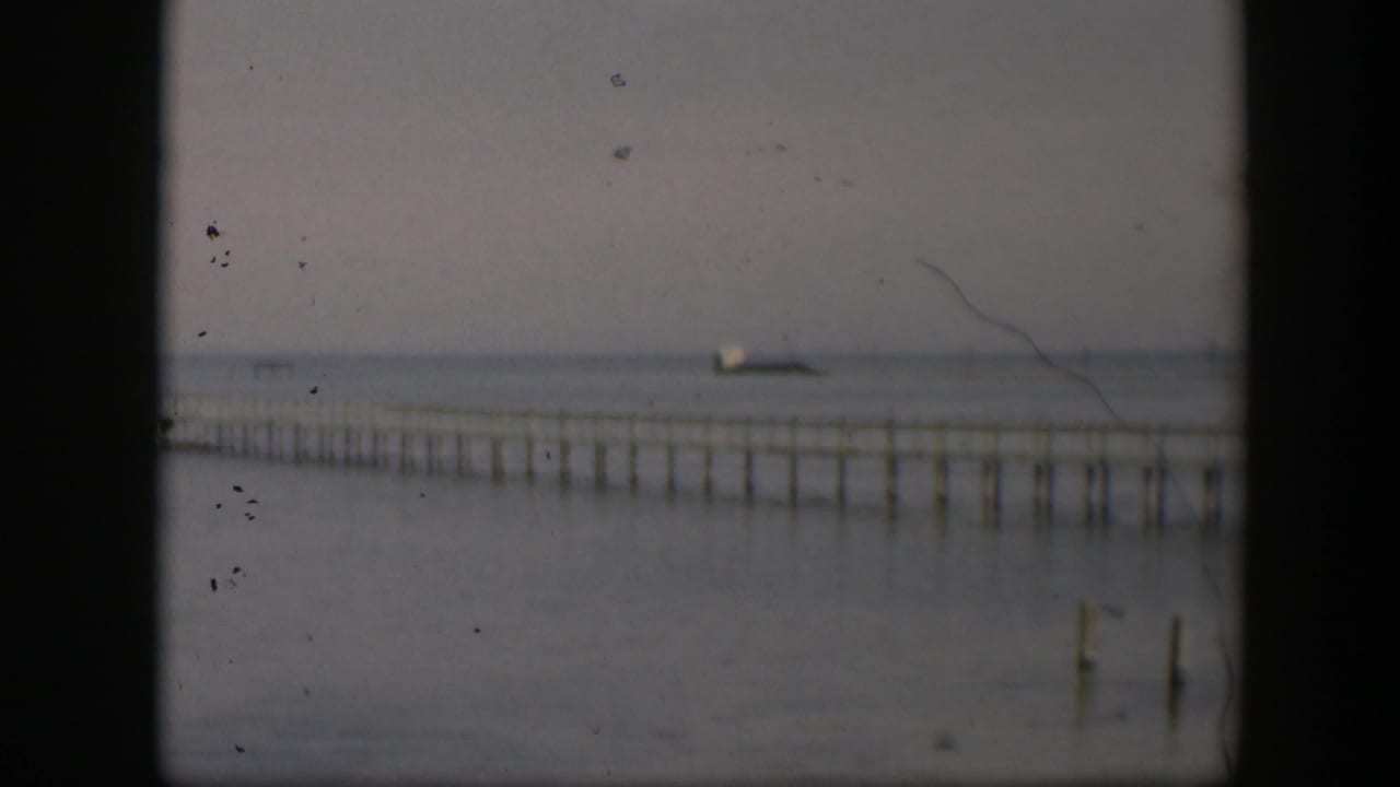 1951 Utah 8mm frame showing the pier lower in the frame, its pilings reflected or silhouetted against calm water and haze.