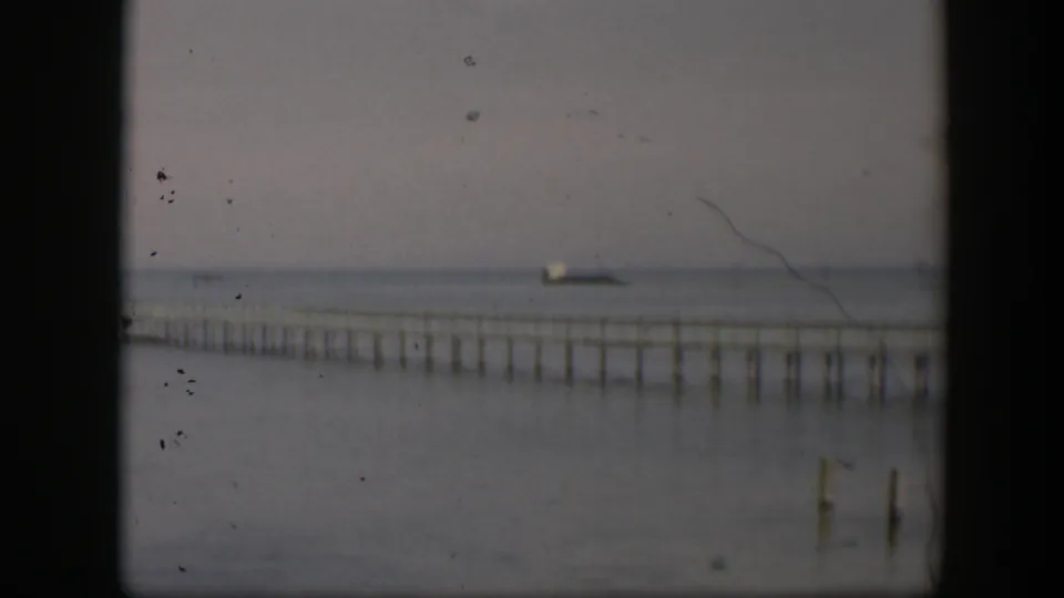 1951 Utah 8mm frame showing the pier lower in the frame, its pilings reflected or silhouetted against calm water and haze.