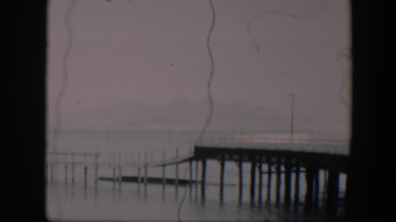 Wooden pier on pilings extending over calm water beneath a hazy sky.