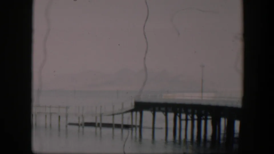 1951 Utah metadata frame showing a wooden pier over still water, with thin posts, a hazy horizon, and aged 8mm film scratches.
