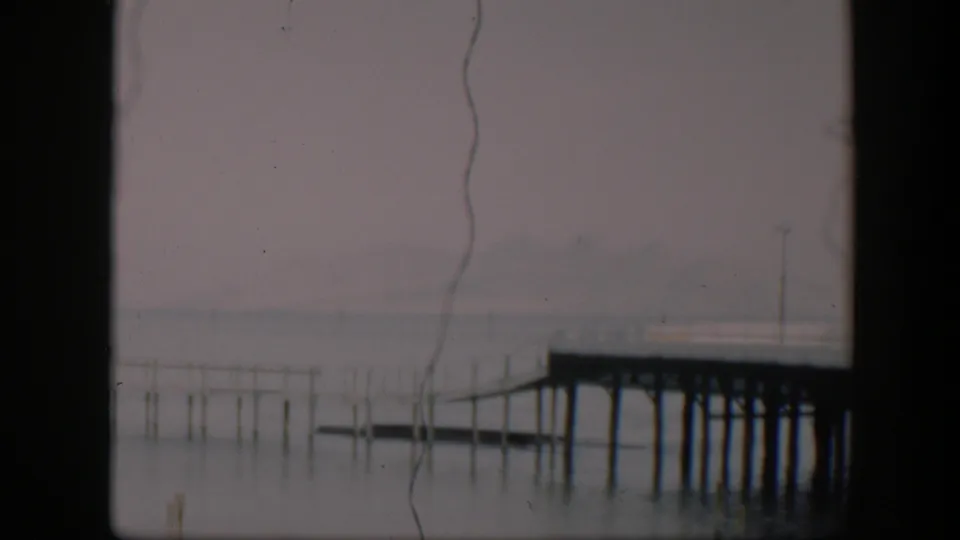 A steady 1951 Utah waterfront view with a wooden pier, scattered posts in the water, muted sky, and visible film wear.