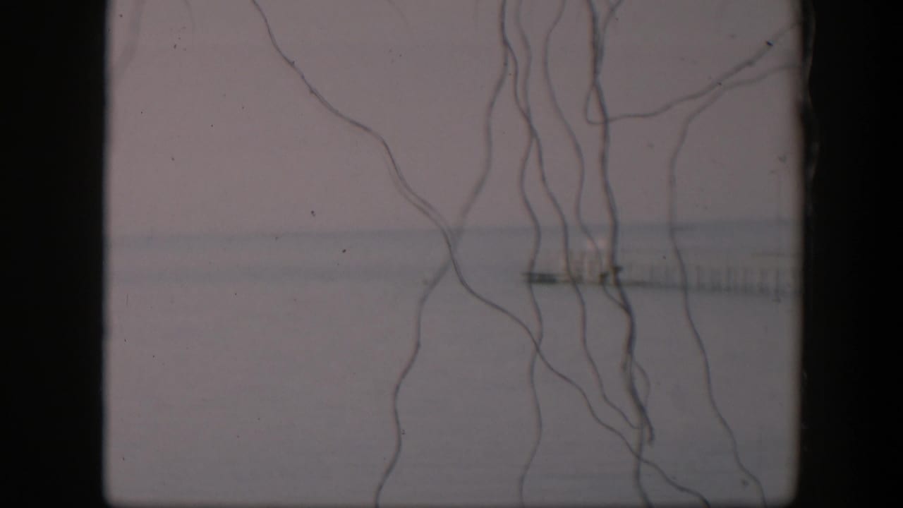1951 Utah 8mm frame with loose foreground strings over a soft gray-white horizon and a small distant pier-like form.