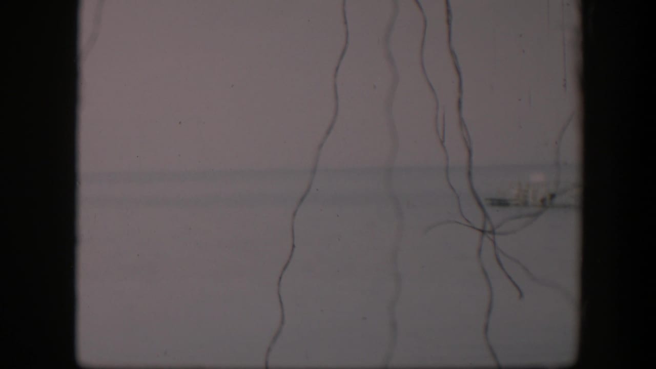 1951 Utah 8mm view of delicate strings against a faded gray background, with a small distant structure near the horizon.
