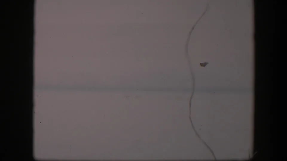 1951 Utah 8mm frame with a faint lake or horizon line, visible scratches, dust, and a prominent vertical tear.