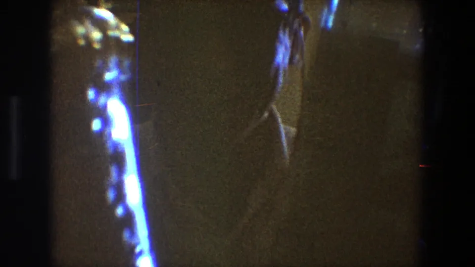 The 8mm frame emphasizes bright reflected light on bottles while the man is mostly hidden in the dim home interior.