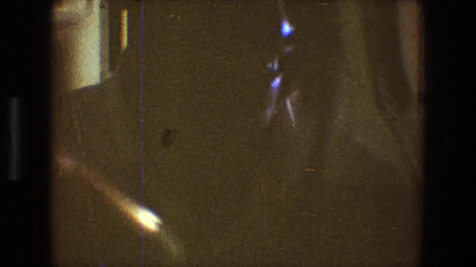 At the end of the Toledo 1968 home-movie clip, the man carries bottles through a shadowed kitchen or dining area.