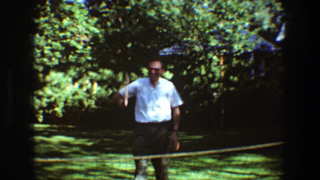 Man in a white shirt stands behind a badminton net on a sunny lawn.