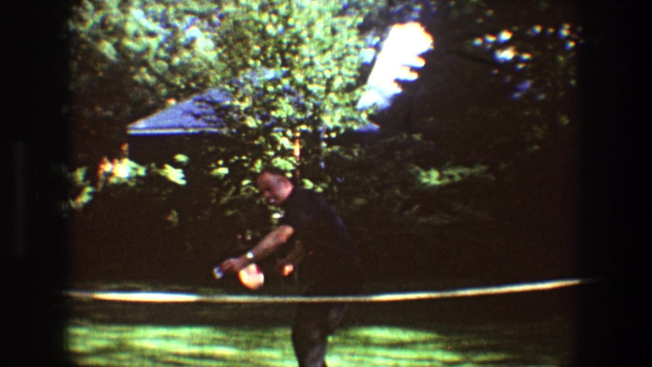 Man bends forward with a badminton racket near the net in a sunny backyard.