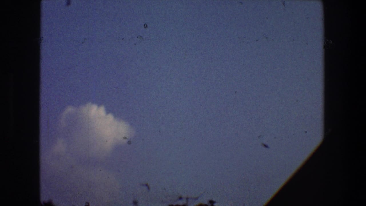 Pale blue sky with a small white cloud, dark film edges, and faint silhouettes along the lower edge.