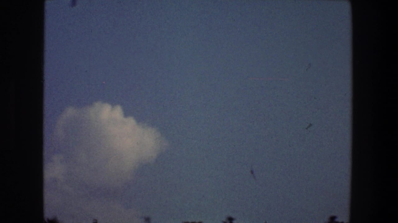 White cloud against blue sky with dark film borders and small specks across the frame.