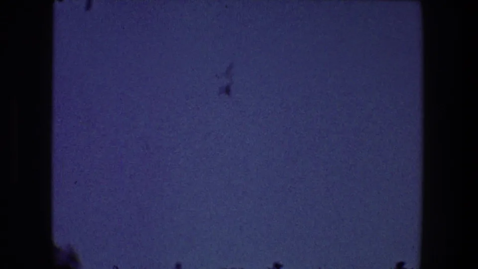 1968 Toledo 8mm frame of mostly open sky with a few distant dark birds or marks, visible grain, and a dark vertical film edge.