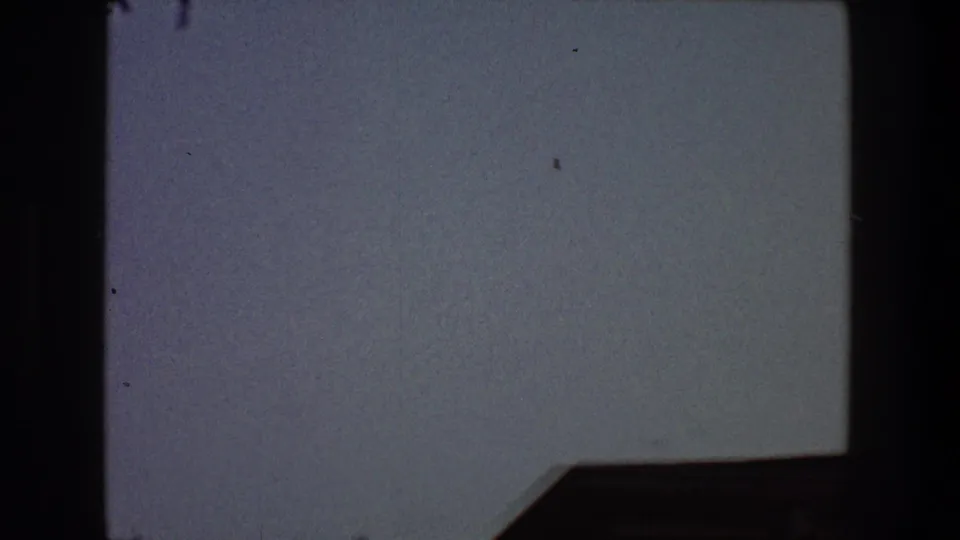 1968 Toledo 8mm frame of open sky with dark gate borders, film specks, and an indistinct angular shadow at lower right.