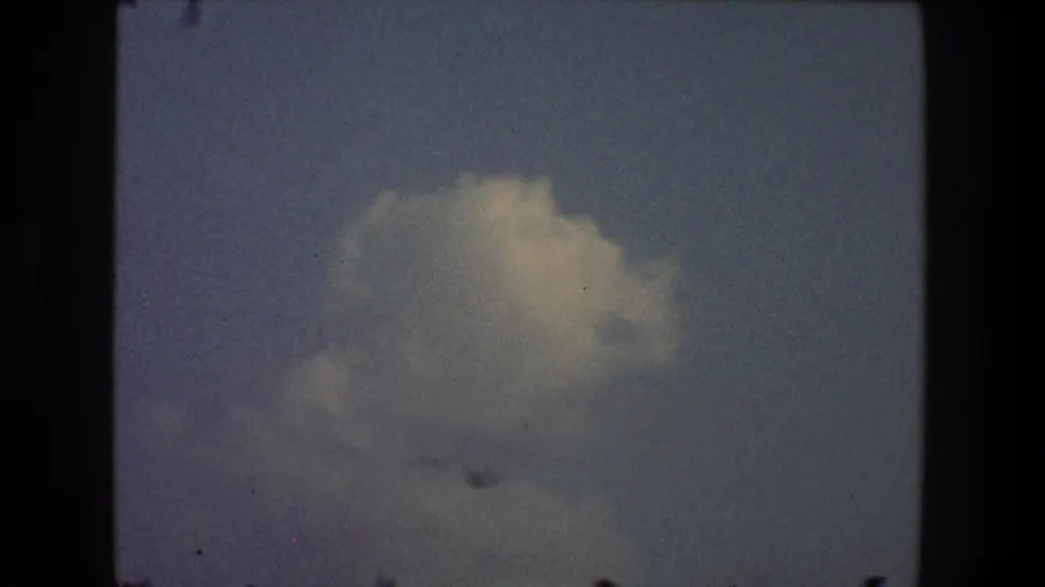 1968 Toledo 8mm frame showing a pale cloud in blue-gray sky, with visible film grain, dust, and dark borders.