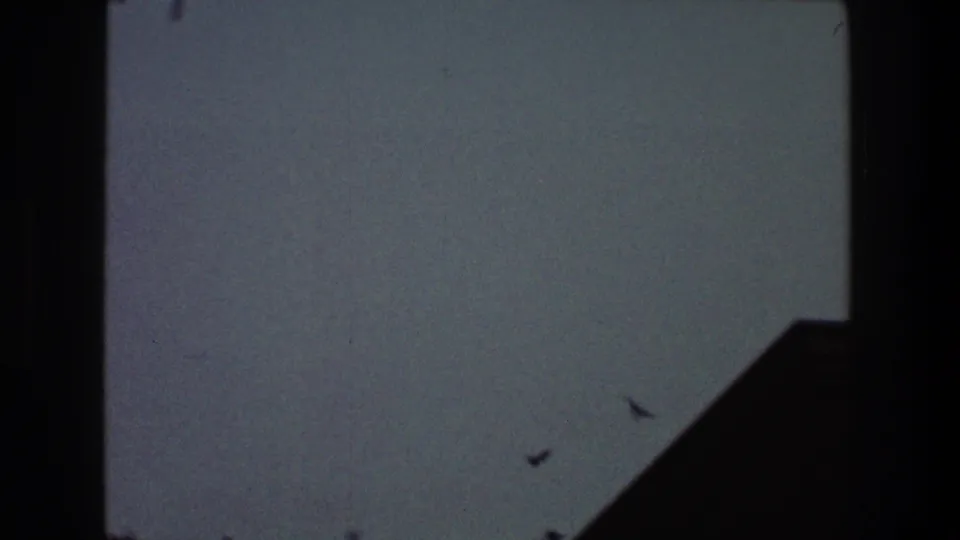 1968 Toledo 8mm frame with small birds visible as dark specks against blue-gray sky near an indistinct angular edge.