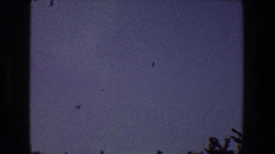 A grainy 8mm dusk frame from the Toledo, Ohio clip shows a mostly open blue-purple sky with faint marks and dark foliage or roof detail along the lower edge.