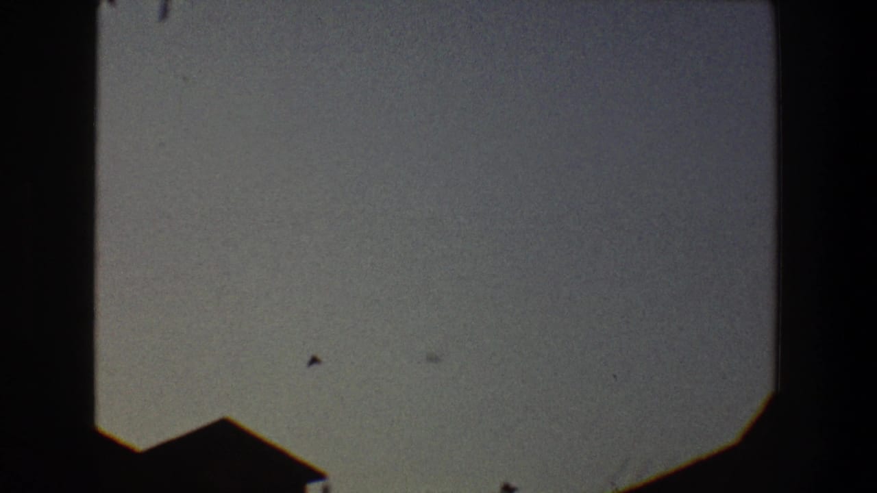 1968 Toledo 8mm frame showing a small bird silhouette in a pale sky above a dark roof edge.