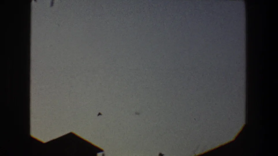 1968 Toledo 8mm frame showing a small bird silhouette in a pale sky above a dark roof edge.
