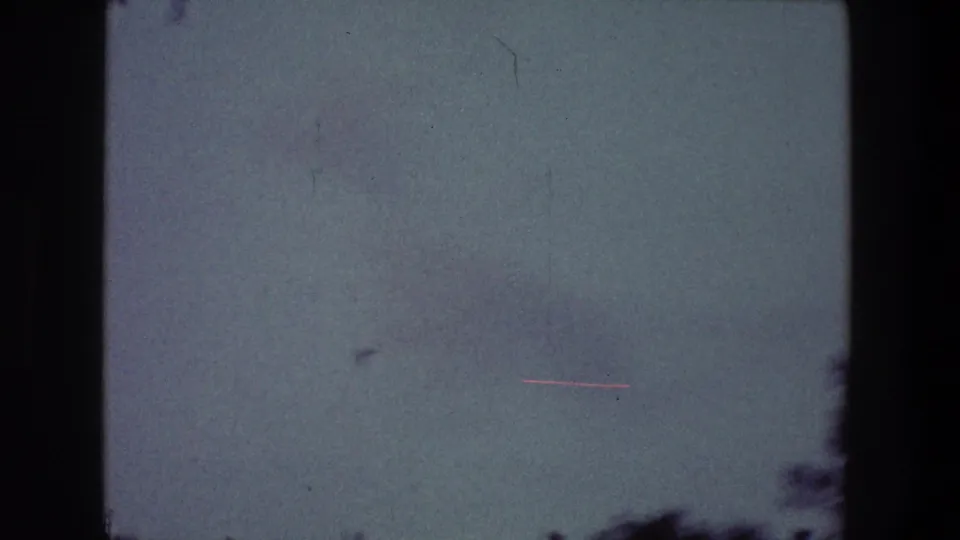 Pale blue-green sky with visible dust, scratch marks, and soft 8mm texture in the 1968 Toledo home-movie clip.