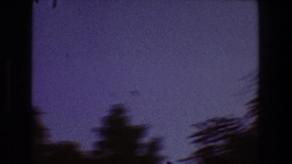 1968 Toledo 8mm frame showing blurred tree tops along the lower edge beneath a grainy purple-blue sky.