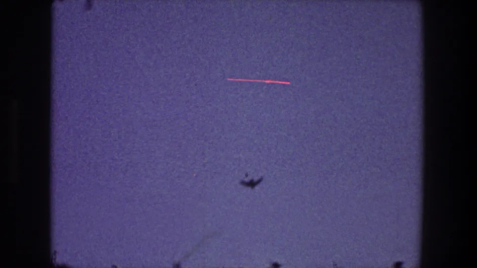 A small bird silhouette crosses the lower portion of a blue-purple sky in this 1968 Toledo 8mm home-movie frame, with faint treetop edges and film wear visible.