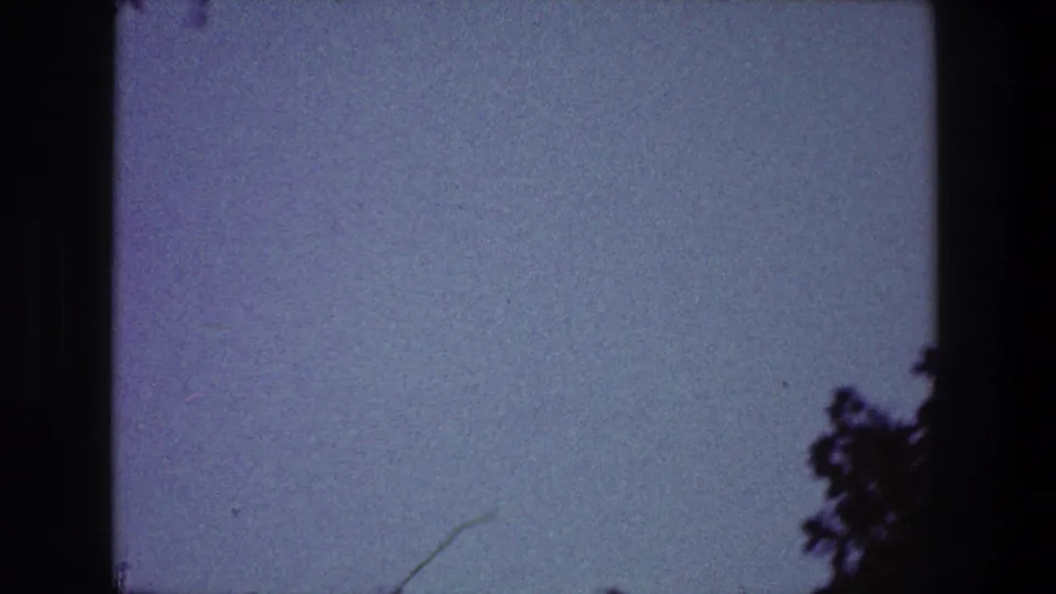 1968 Toledo home-movie frame with open blue sky, dark tree silhouettes at the edge, and visible 8mm frame borders.