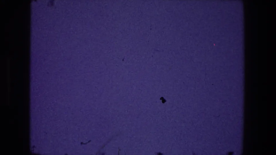1968 Toledo 8mm frame with a quiet blue-purple exposure, grain, dust marks, and a small dark speck near the upper right.
