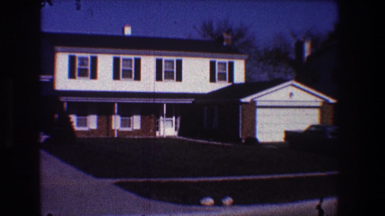 Two-story suburban house with dark shutters, attached garage, lawn, and driveway.