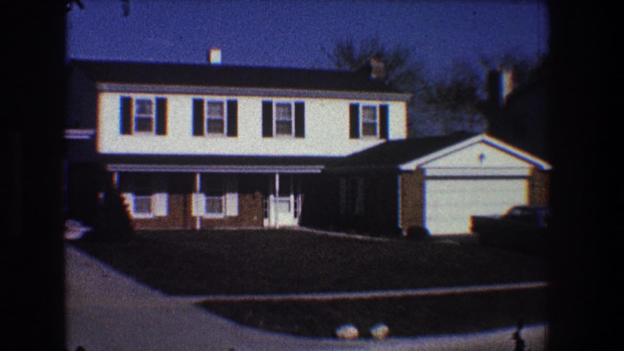 Suburban house exterior with attached garage, porch, lawn, and a dark car at right.