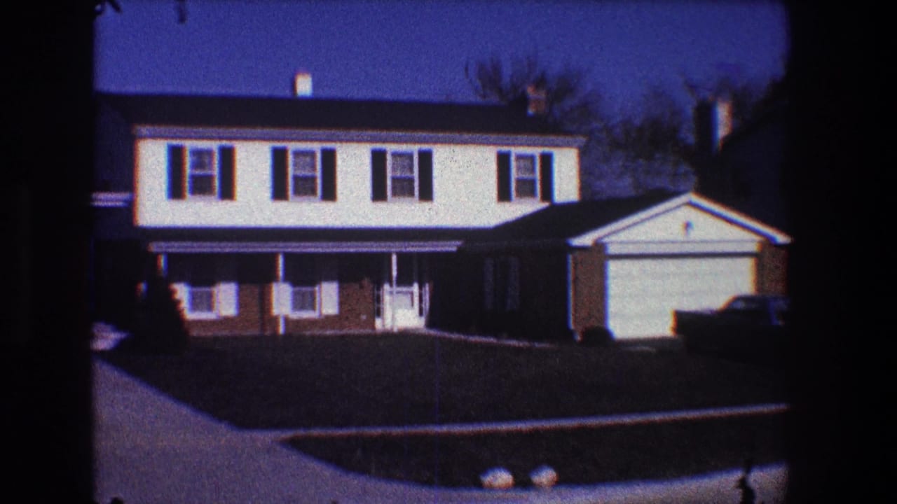 Suburban house front with attached garage, dark shutters, driveway, and parked car.