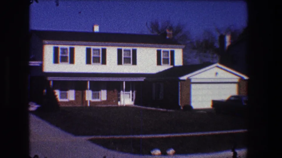 1968 Toledo frame showing the front of a suburban residence with white upper siding, brick lower level, attached garage, and street curb.