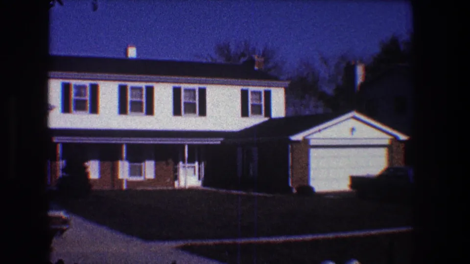 Late-1960s Toledo frame showing the same suburban house exterior with garage, lawn, driveway, and deep blue sky.