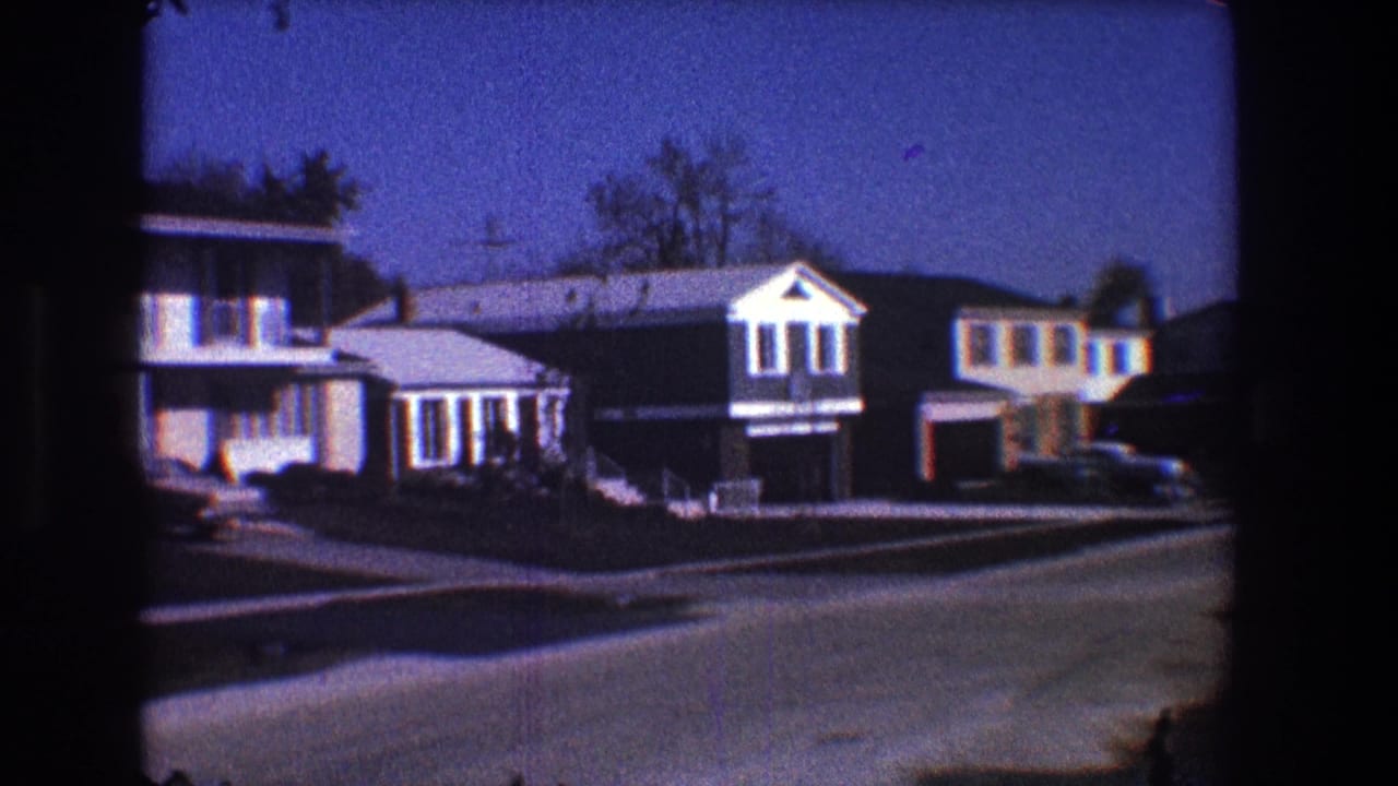 Houses with garages and parked cars beside a curving residential street.