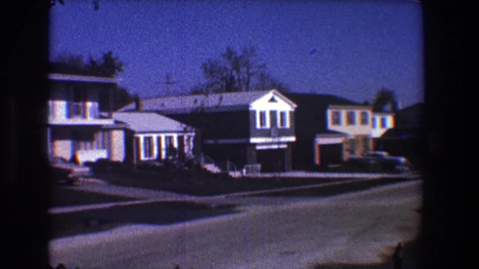 Street-level 8mm view of Toledo suburban homes with attached garages, parked automobiles, lawns, and late-day shadows.