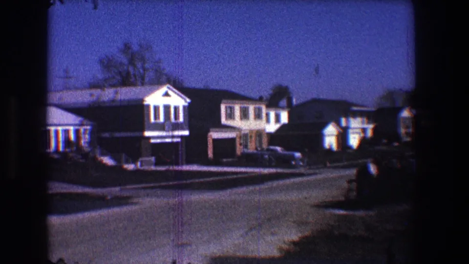 1968 Toledo frame with a row of suburban houses, driveways, parked cars, rooftops, bare trees, and a darkened foreground.