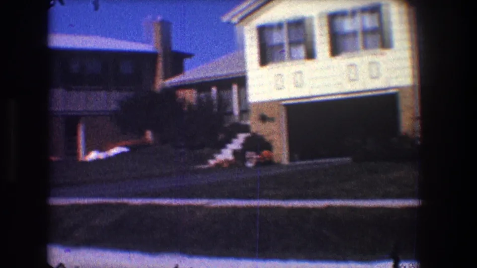 1968 Toledo suburban street view with neighboring houses, attached garage, chimney, lawn, shrubs, and small patches of snow.
