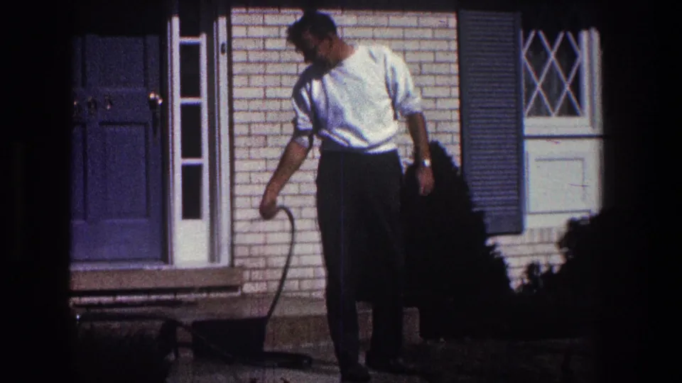 The man remains near the brick porch in the 1968 Toledo home-movie footage, holding the hose wand toward the ground.