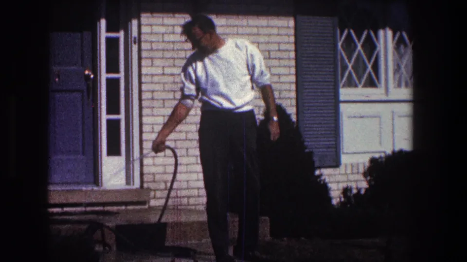 A 1968 Toledo exterior frame shows the man beside a brick house, with a white-trimmed window and blue shutter behind him.