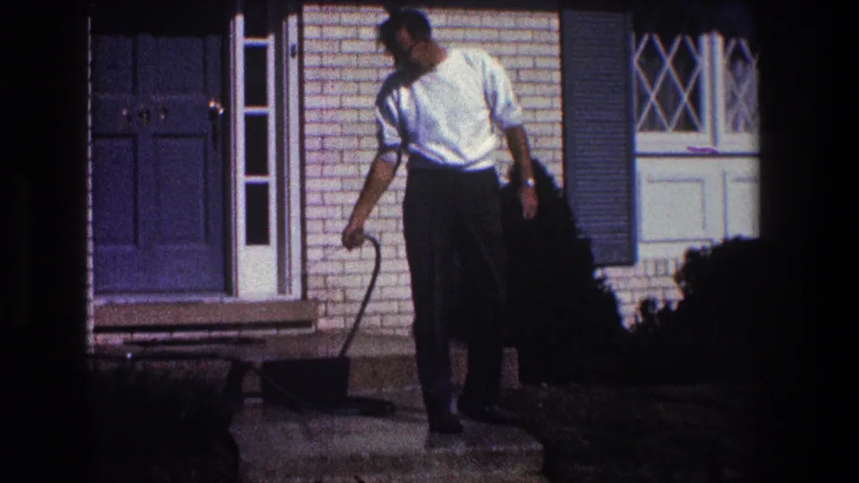 In 1968 Toledo home-movie footage, a man in a white shirt stands by the front steps of a brick house while cleaning with a hose.