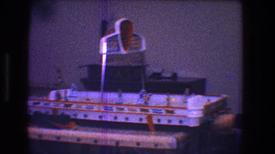1968 Toledo home-movie frame showing the tabletop hockey board in a dim interior, with miniature players, orange details, and the central goal visible.