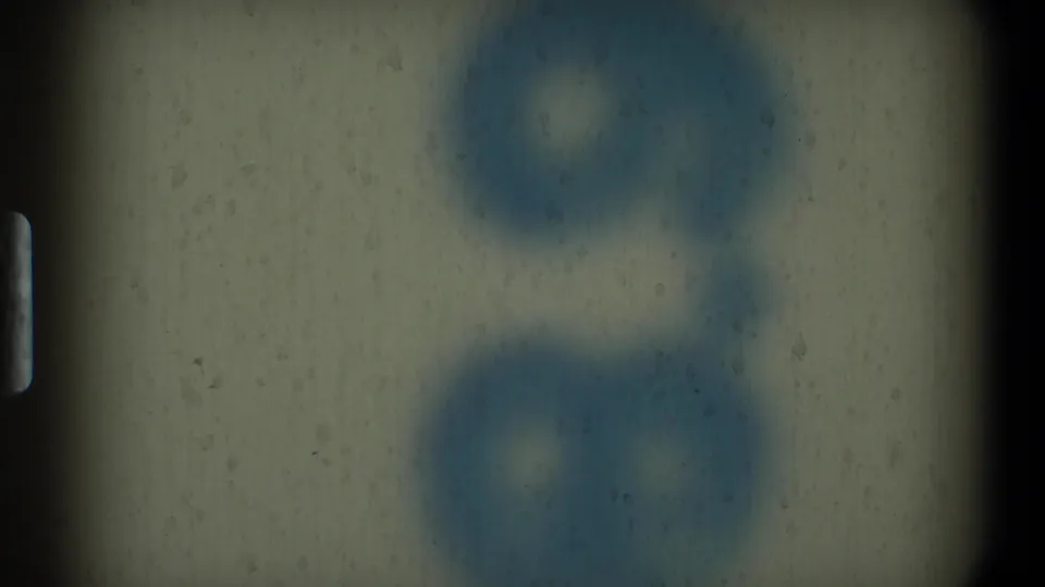 A soft 8mm home-movie frame shows an out-of-focus textured interior surface with blue shapes and visible grain.