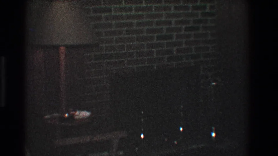 1968 Toledo home-movie frame showing a brick chimney or fireplace area, small table, and indistinct objects in low light.