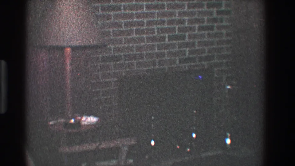 1968 Toledo 8mm frame of a dim brick chimney or fireplace area with a small table and soft color flecks from the film scan.